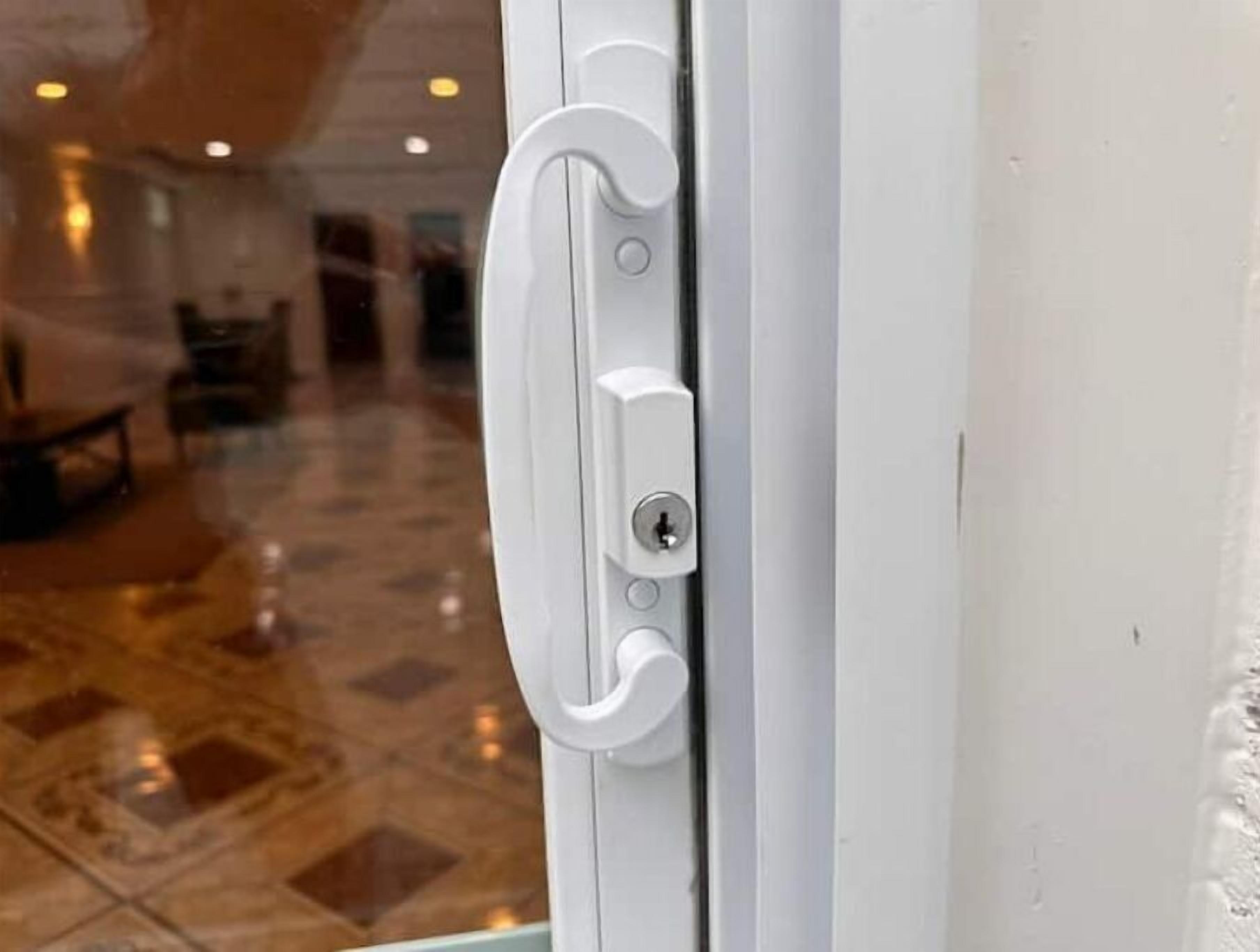 Una maniglia bianca con una serratura, parte di una porta in un edificio con pavimento piastrellato e uno spazio interno visibile.