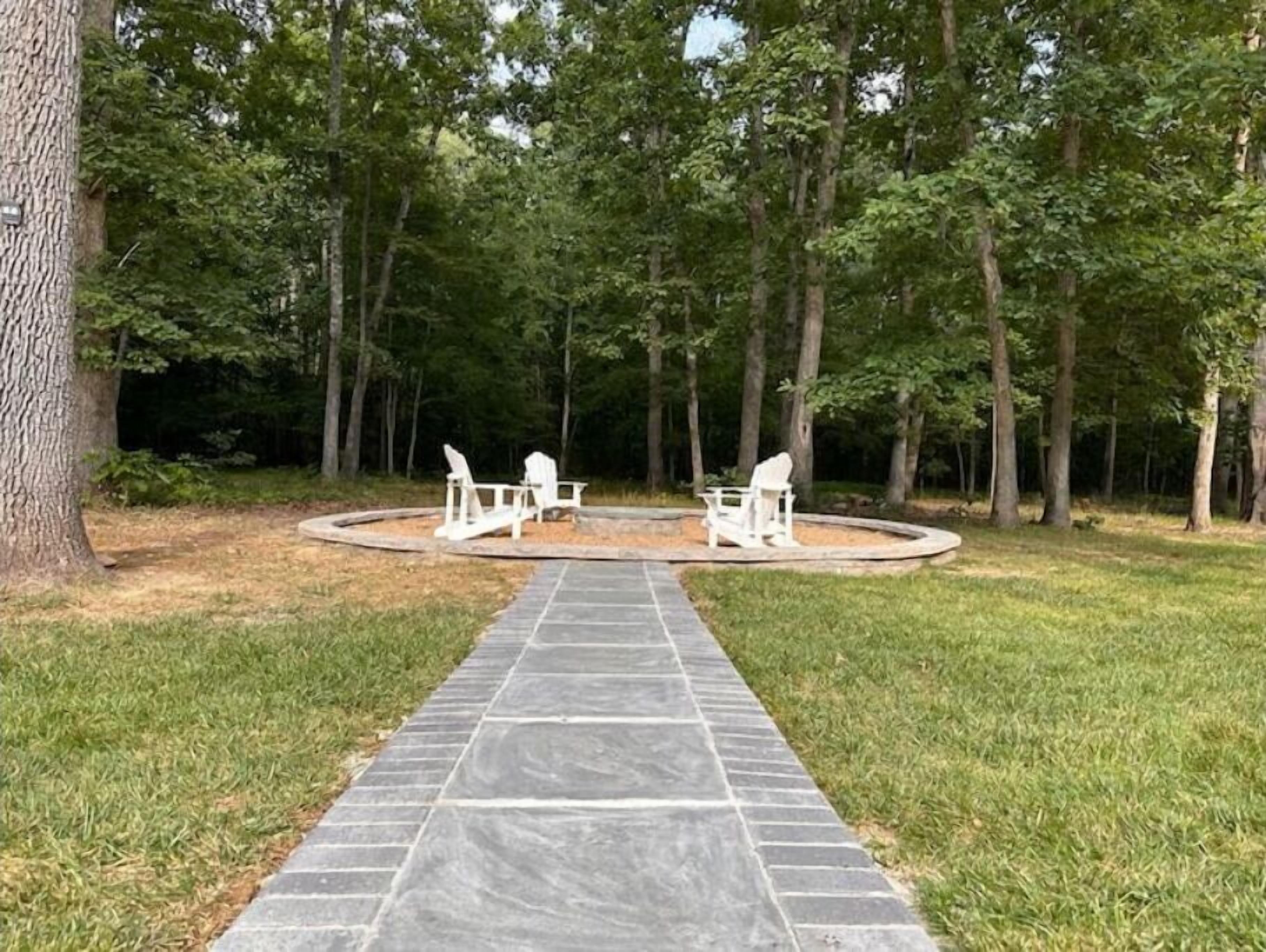 A stone pathway leading to a circular seating area with Adirondack chairs in a wooded setting.