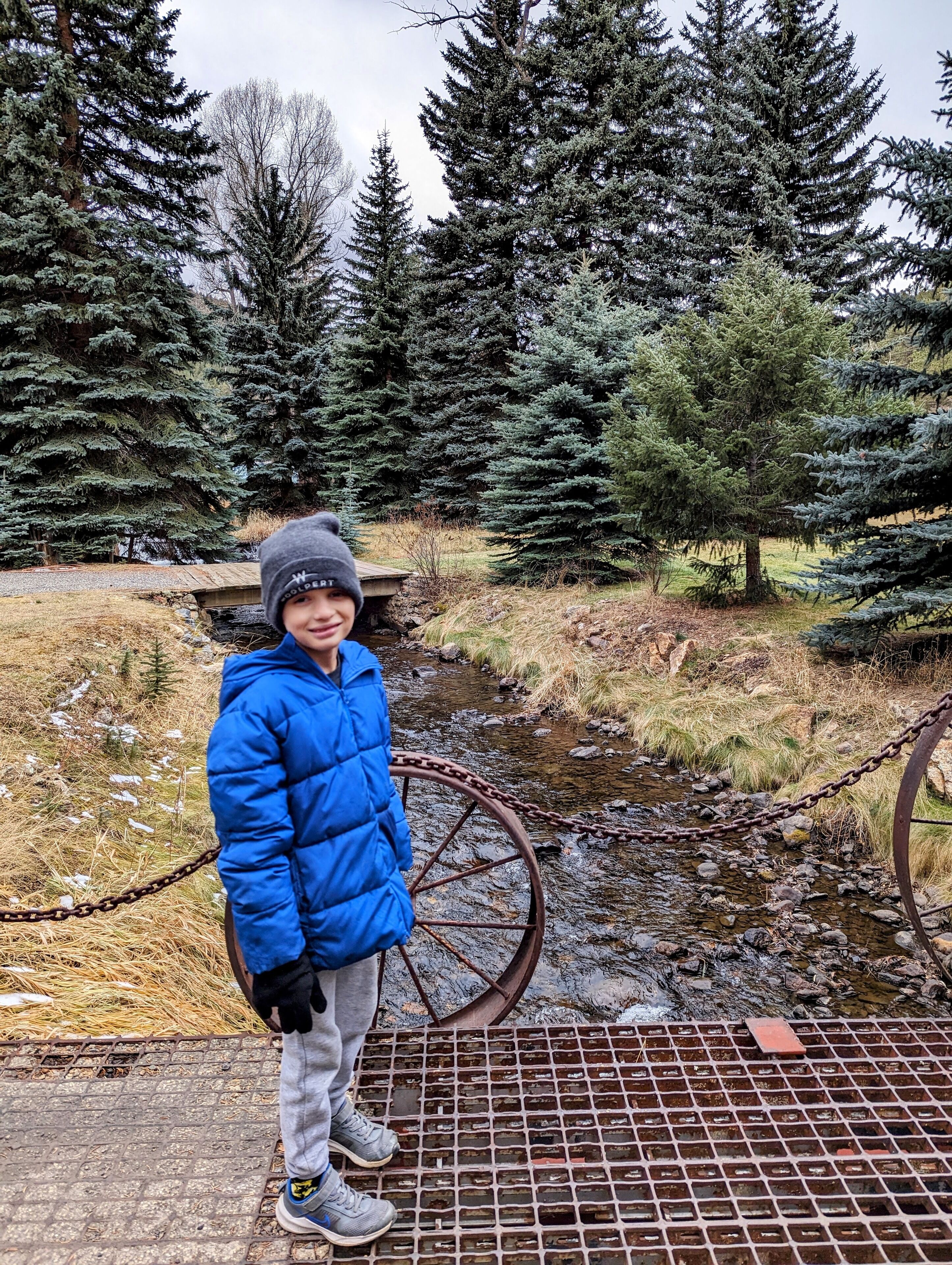 A person standing on a metal grate over a stream, surrounded by coniferous trees.