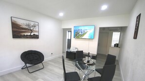 A modern room with a glass table, black chairs, a mounted TV displaying a welcome message, and a framed landscape painting on the wall. - Diaz Stay Miami Airport (Miami)