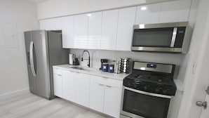 A modern kitchen with white cabinets, a stainless steel refrigerator, a microwave, and a gas stove. - Diaz Stay Miami Airport (Miami)