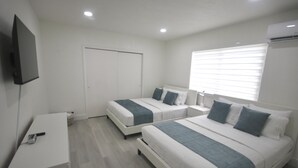 A modern bedroom with two beds, a TV, and a window with blinds. - Diaz Stay Miami Airport (Miami)