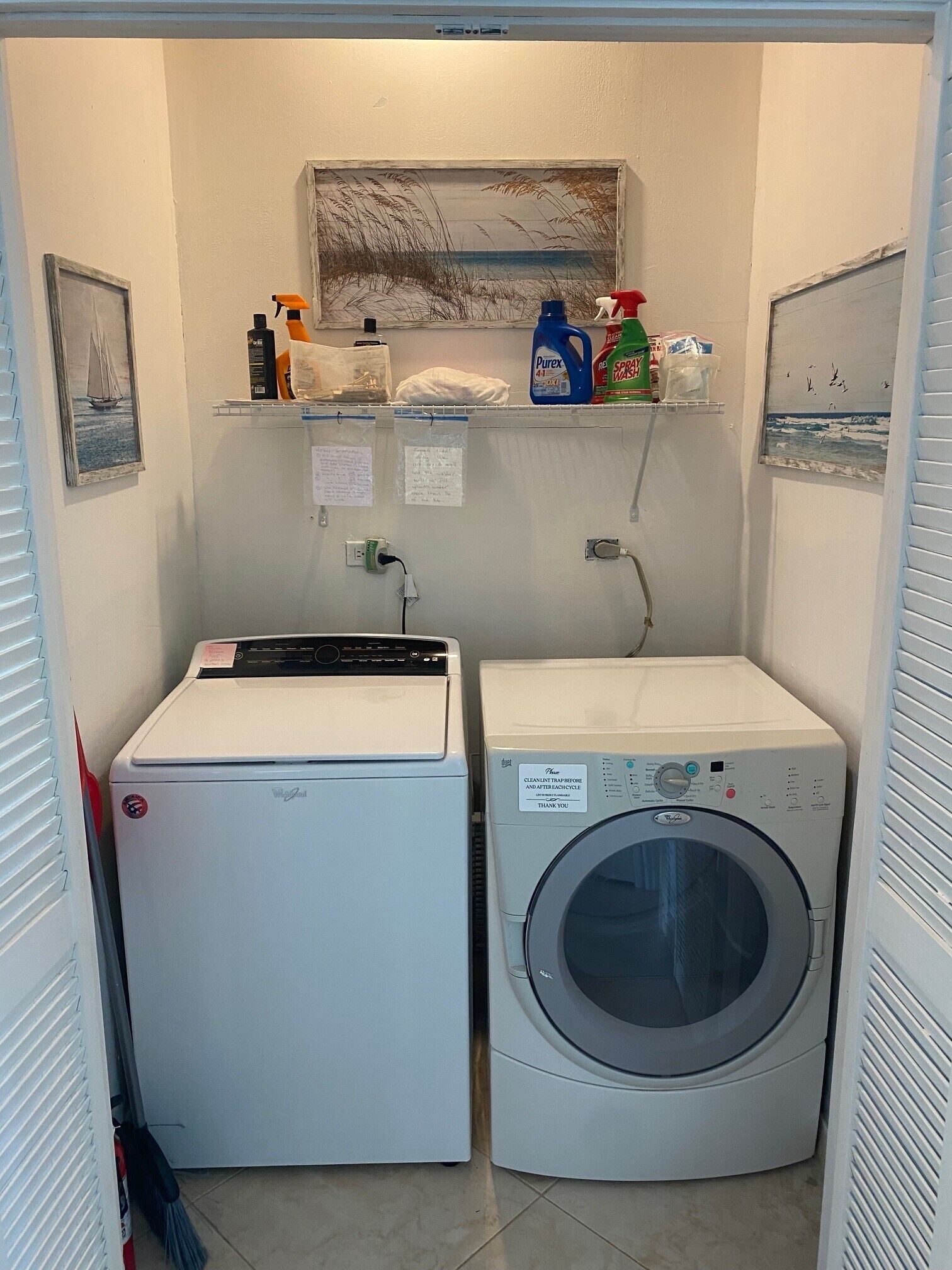 A compact laundry room with a washing machine and dryer, a shelf with cleaning supplies, and a small painting on the wall.