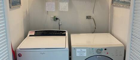A compact laundry room with a washing machine and dryer, a shelf with cleaning supplies, and a small painting on the wall.