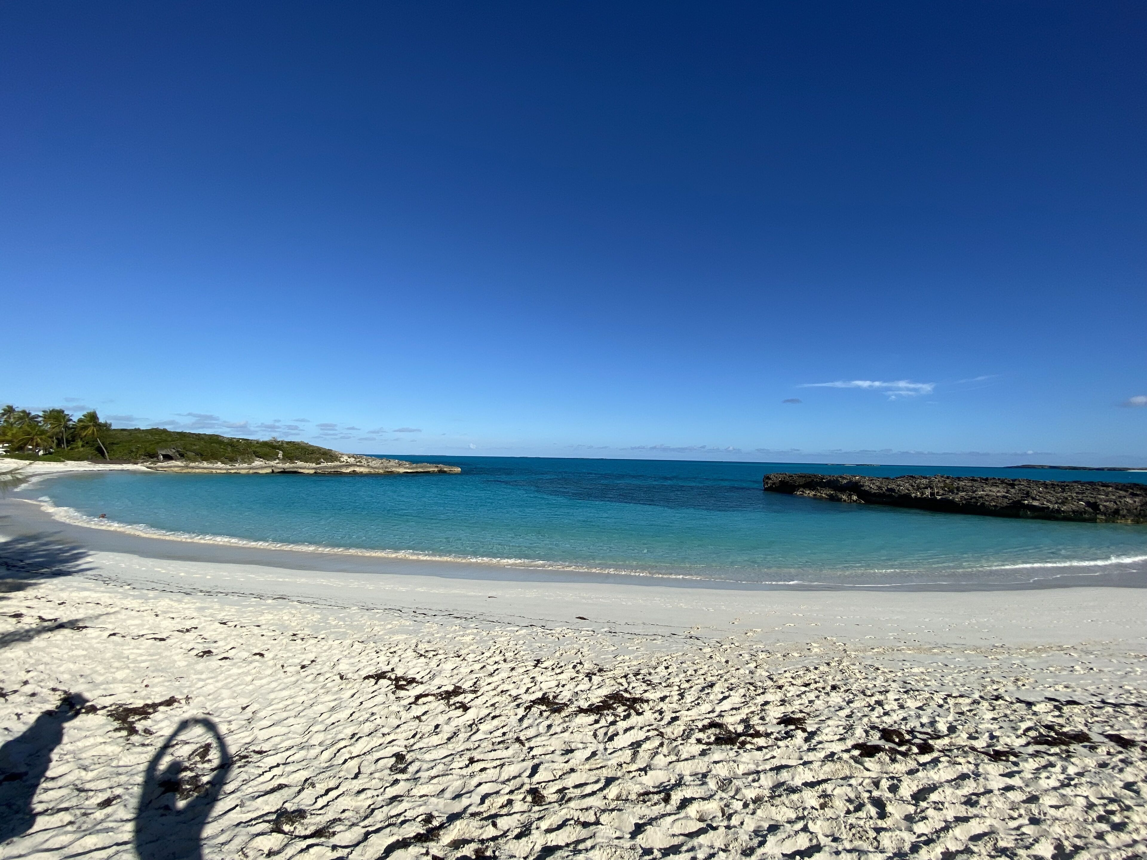 En strand med klart, blåt vand, hvidt sand og en klippeudspringning.