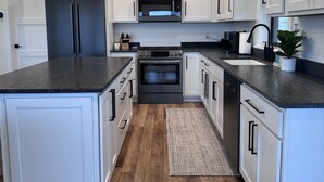 A modern kitchen with white cabinets, a stainless steel refrigerator, a built-in microwave, a stove, and a black countertop. - Modern Farmhouse with Breathtaking Views! (Bozeman)