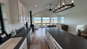 A modern kitchen with a large island, white cabinetry, and a view of a field through large windows. - Modern Farmhouse with Breathtaking Views! (Bozeman)