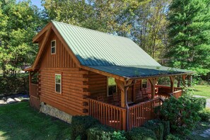Eine Blockhütte mit grüner Metallen Dach, einer Veranda mit Holzgeländern und einem Steinfundament.