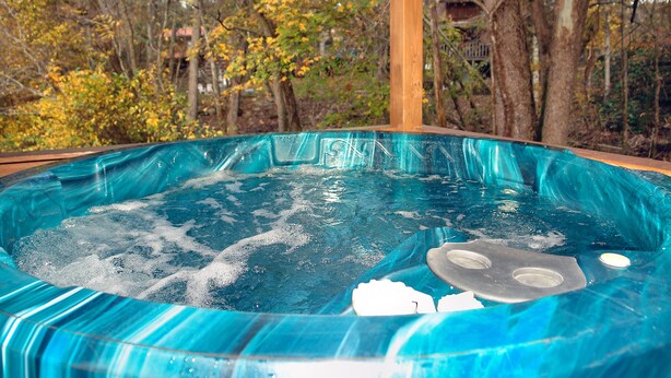 Een hottub met een helderblauw interieur, omgeven door bomen en een houten constructie.