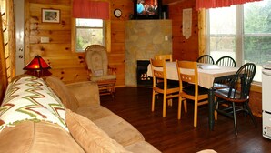Een gezellig chaletinterieur met een bank, eettafel, stoelen, een open haard en een televisie.
