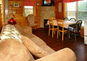 A cozy cabin interior with a sofa, dining table, chairs, a fireplace, and a television. - Jon's Pond on Cosby Creek (Cosby)