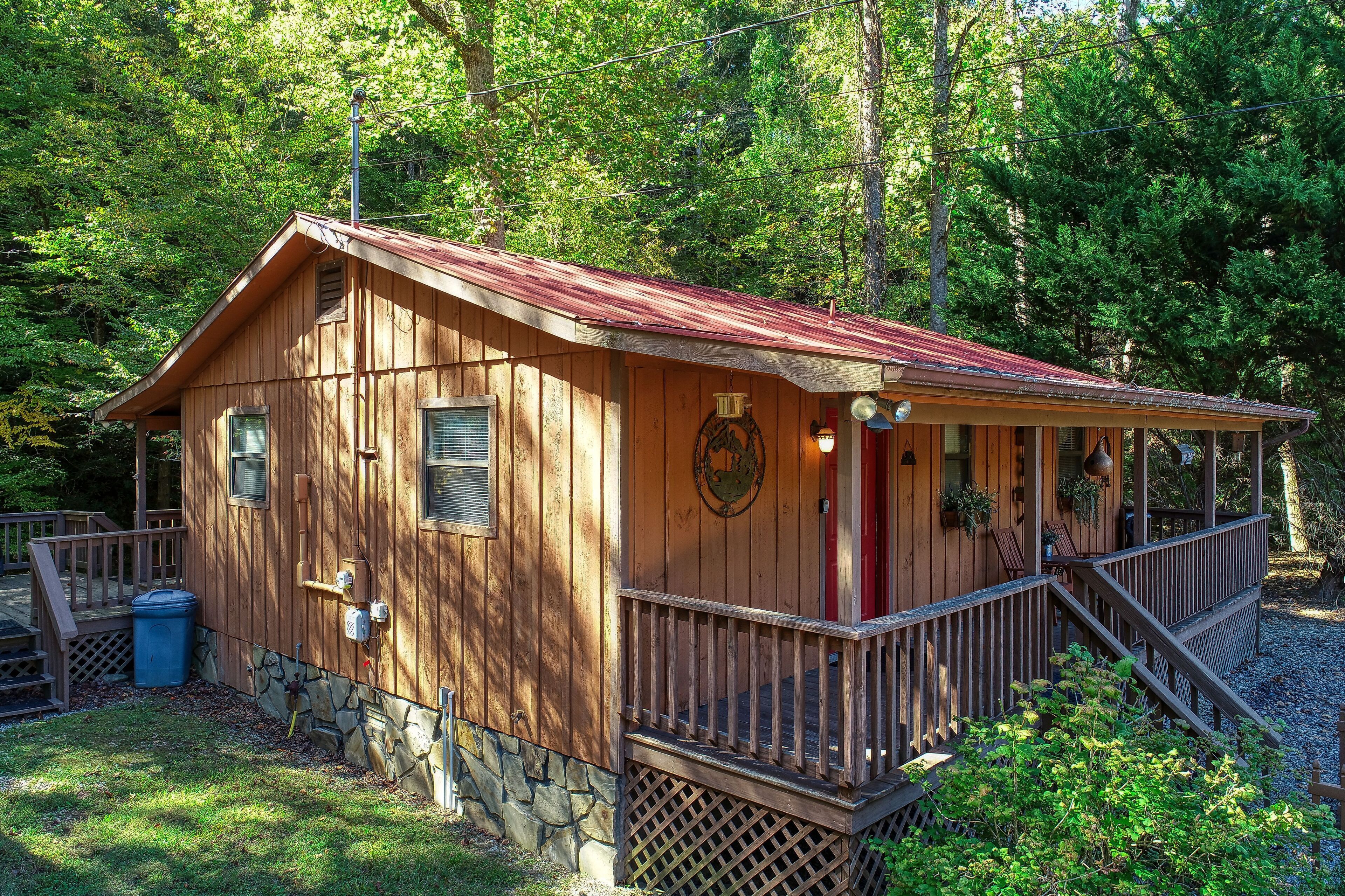 A wooden cabin with a porch, stone foundation, and a red roof.