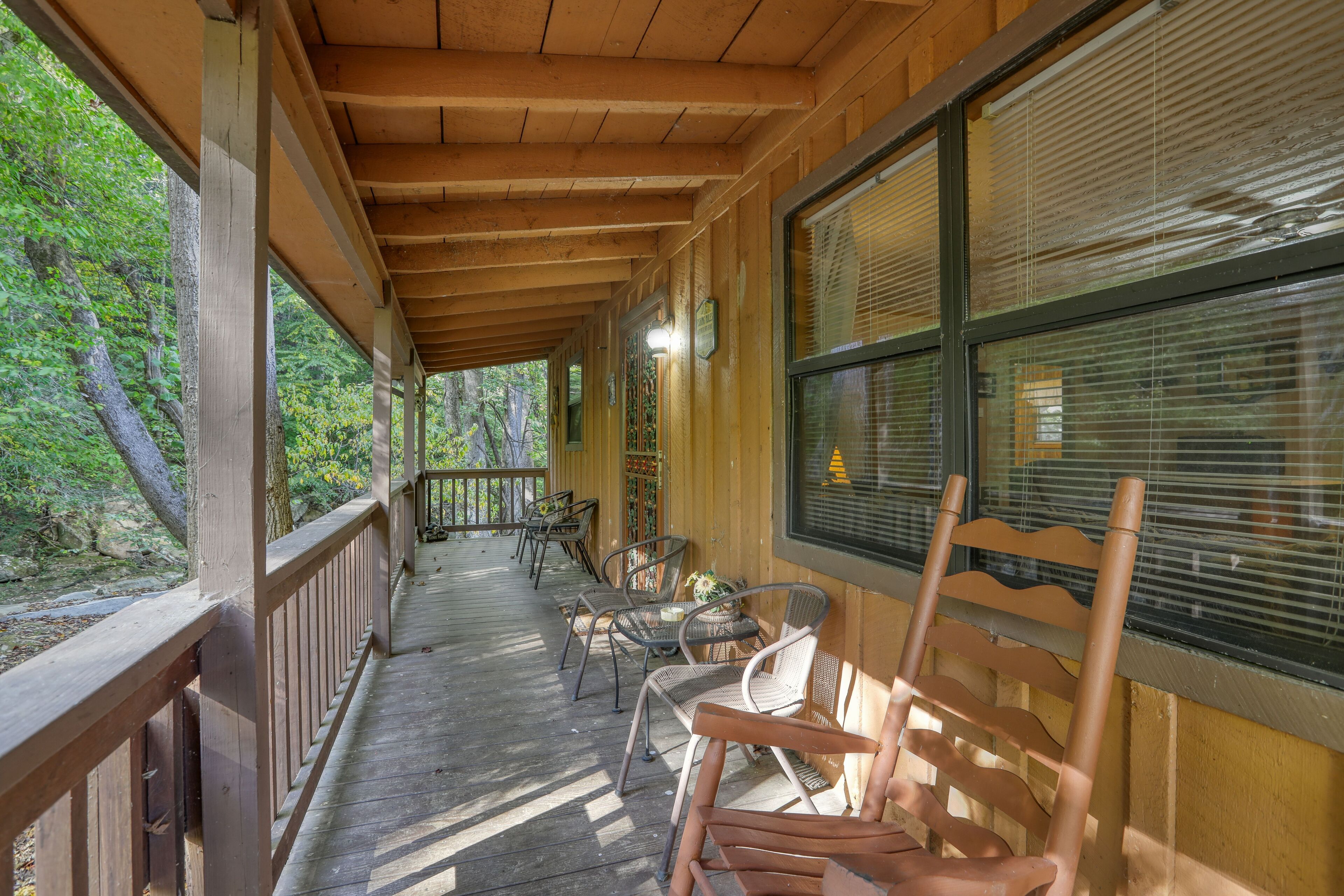 A covered porch with wooden railings, a row of chairs, and a view of the forest.