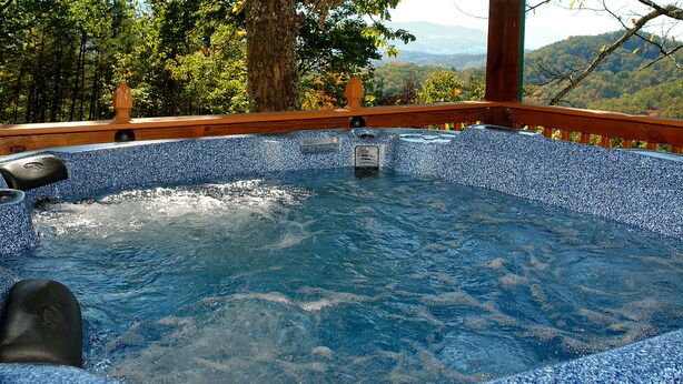 Un bain à remous avec une terrasse en bois et une vue sur une chaîne de montagnes boisée.