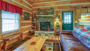 A cozy cabin interior with a stone fireplace, wooden walls, a leather couch, and a dining table.