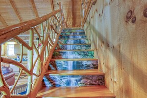 A wooden staircase with a wooden railing and a view of a kitchen area. - Bear Pause Cabin in the Smokies! (Sevierville)