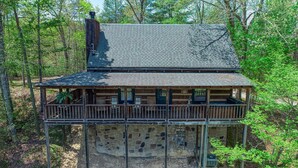 A two-story cabin with a stone foundation, a wooden deck, and a chimney.