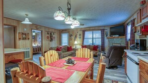 Interior acolhedor de uma cabana com uma mesa de jantar de madeira, cadeiras, um sofá e uma cozinha.