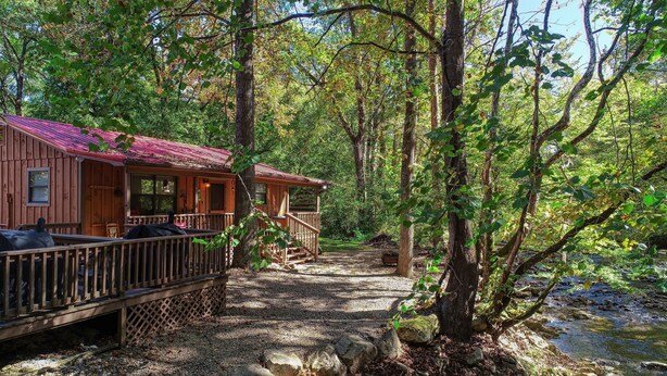 Uma cabana com deck de madeira e varanda, rodeada por árvores e um riacho.