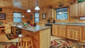 A wooden cabin interior with a kitchen area featuring wooden cabinets, a bar stool, and a dining table. - Elk Run is a stunning, two bedroom cabin situated directly on Cosby Creek. (Cosby)