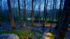 A forested area with a stone pathway leading to a small pond surrounded by rocks and illuminated by lanterns. - Elk Run is a stunning, two bedroom cabin situated directly on Cosby Creek. (Cosby)