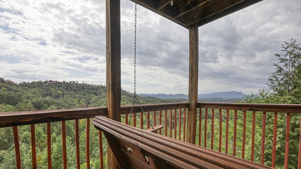 A wooden deck with a bench, overlooking a forested landscape with mountains in the distance. - An Amazing View in Pigeon Forge. (Sevierville)