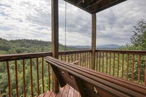 A wooden deck with a bench, overlooking a forested landscape with mountains in the distance. - An Amazing View in Pigeon Forge. (Sevierville)