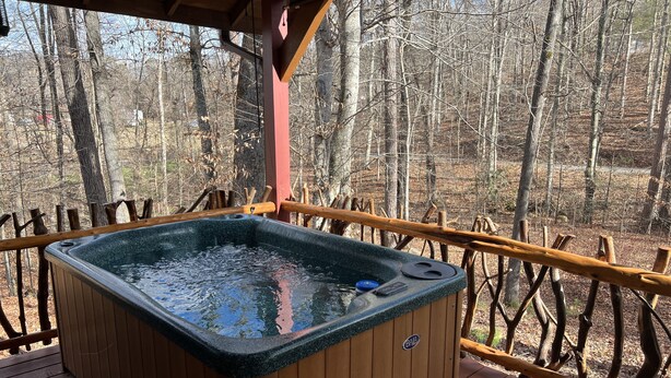 Un bain à remous sur une terrasse en bois, avec vue sur une forêt.