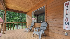 Een houten veranda met twee Adirondack stoelen en een 'WELCOME' bord.