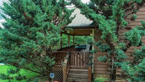 Eine Holzhütte mit einer Veranda, einem Whirlpool und einer Holztreppe, die zur Veranda führt.