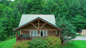 Eine kleine Holzhütte mit Veranda, umgeben von üppigem Grün.