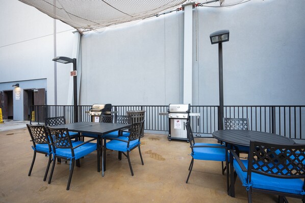An outdoor patio area with tables and chairs, a grill, and a trash can.