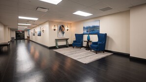 Un hall d’hôtel avec un parquet en bois foncé, des fauteuils bleus, une petite table et des œuvres d’art accrochées au mur.