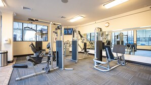 Une salle de sport équipée de divers appareils d’exercice, dotée de grandes fenêtres et d’un sol recouvert de moquette.