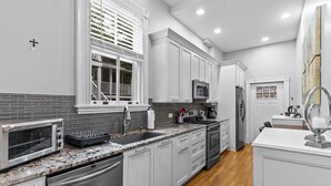 Una cocina moderna con armarios blancos, encimera de granito, electrodomésticos de acero inoxidable y ventana con persianas.