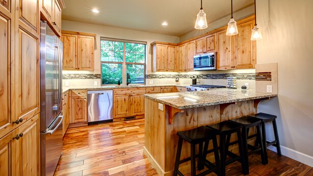 Cocina con armarios de madera, electrodomésticos de acero inoxidable, encimera de granito y ventana con vistas a árboles.
