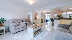 Una sala de estar moderna con un sofá color beige, una mesa de centro blanca y una zona de cocina con barra.