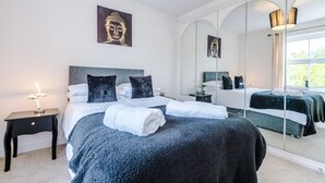 Un dormitorio con una cama grande, una mesita de noche con lámpara, un espejo y obras de arte en la pared.