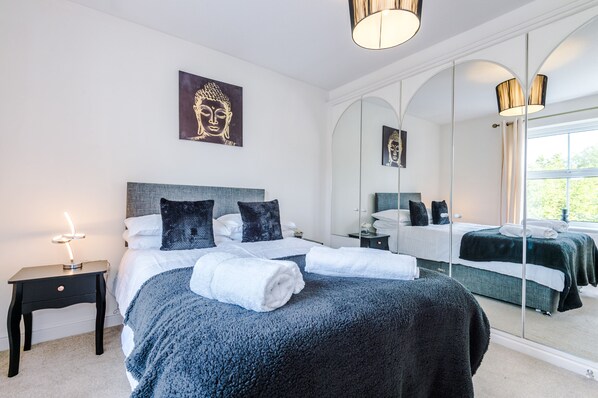 A bedroom with a large bed, a bedside table with a lamp, a mirror, and artwork on the wall. - Detached 5 bed property (Worsley)