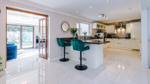 Una cocina moderna con una isla central, dos taburetes de bar y un ventanal grande.