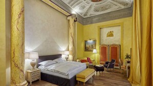 A hotel room with a large bed, a nightstand, a desk, a chair, and a decorative ceiling. - Palazzo di Alcina-Residenza D'Epoca (Bologna)