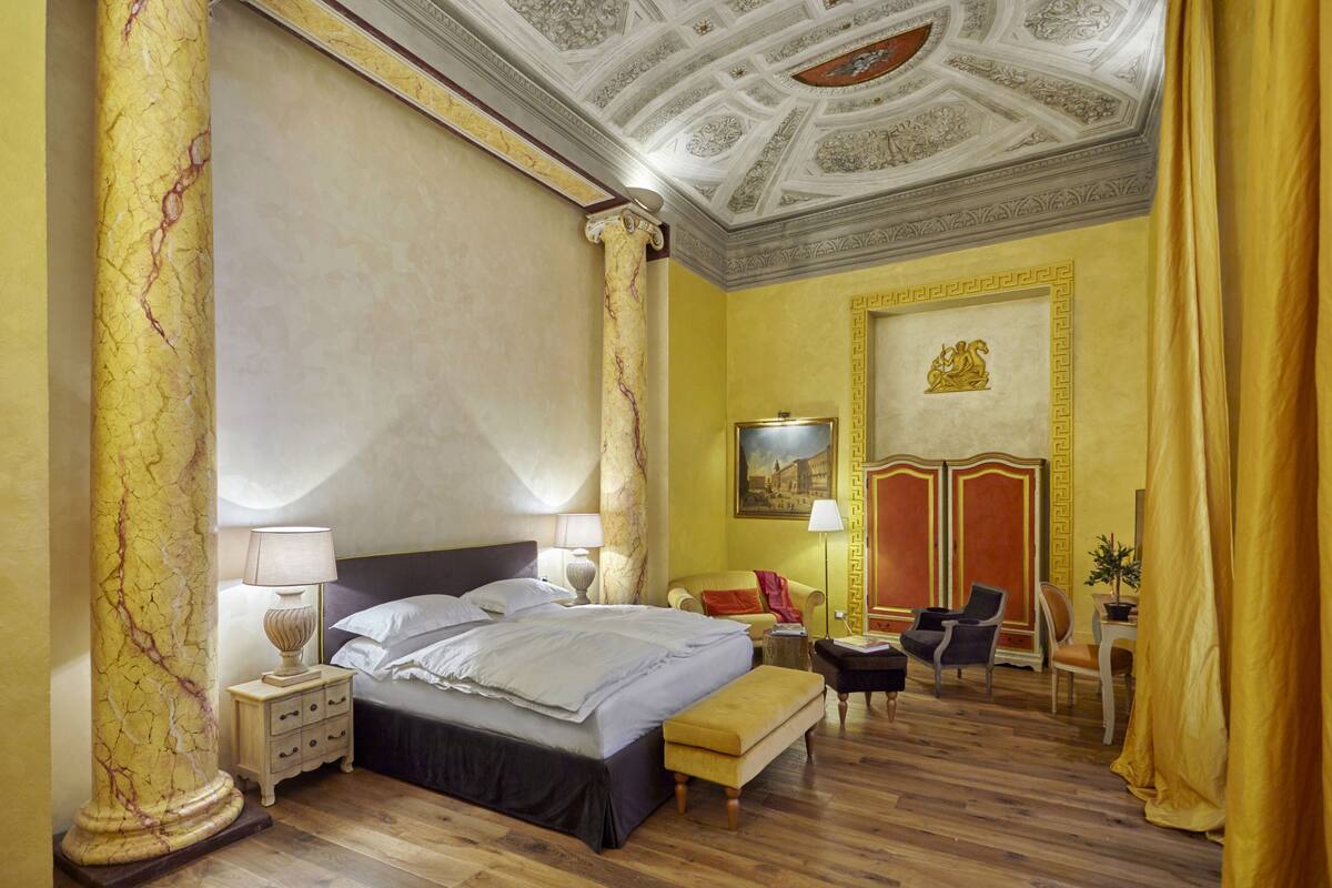 A hotel room with a large bed, a nightstand, a desk, a chair, and a decorative ceiling.
