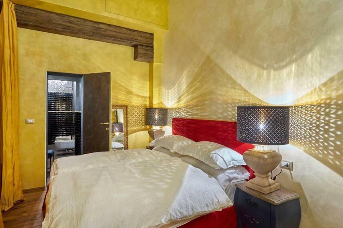 A hotel room with a bed, a nightstand, a lamp, and a red headboard.