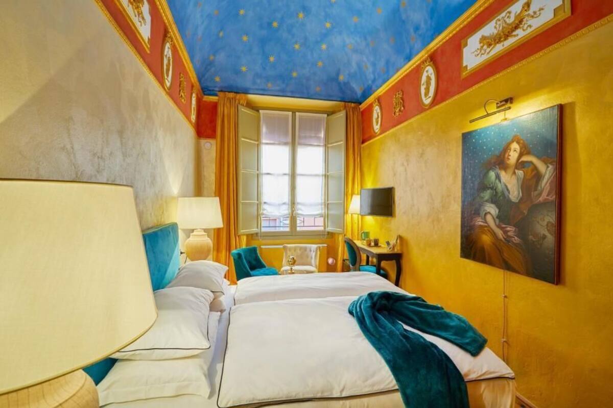 A hotel room with a large bed, two bedside tables, a desk, and a window with curtains.