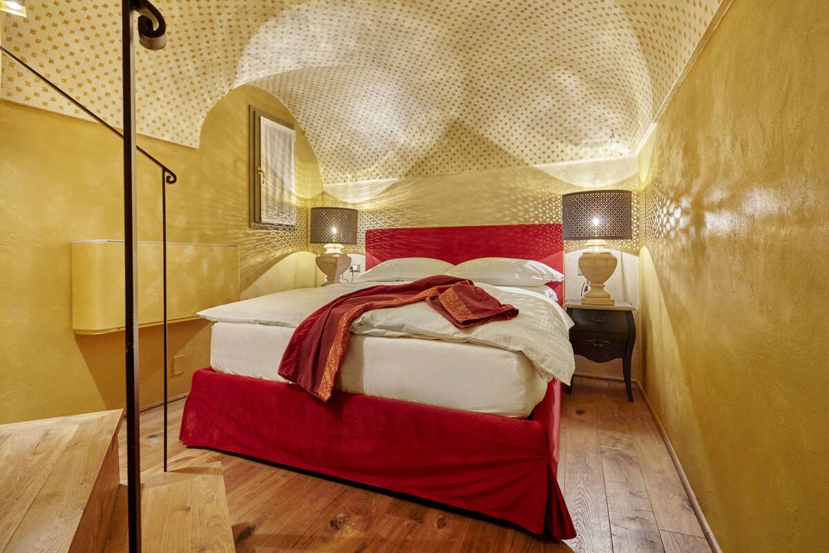 A bedroom with a large bed, wooden flooring, and a red headboard.