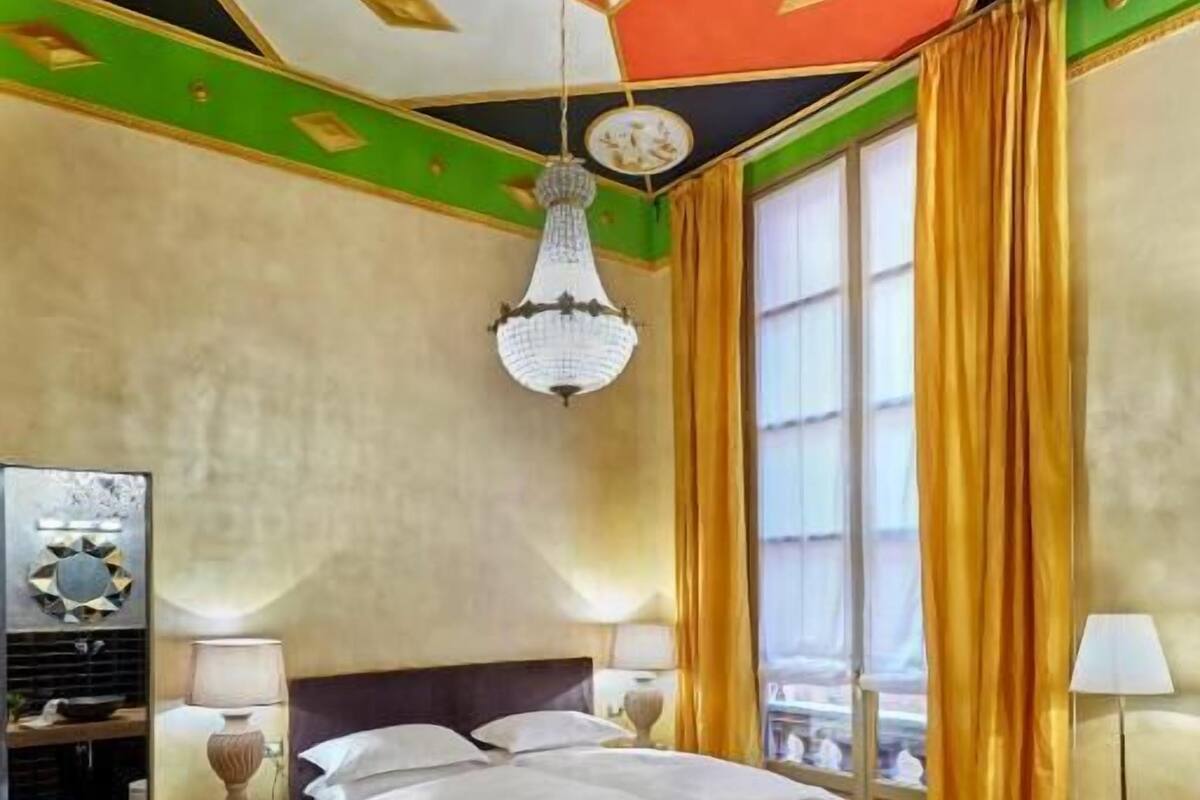 A hotel room with a bed, a round table with a clock, a chair, a dresser, and a mirror.