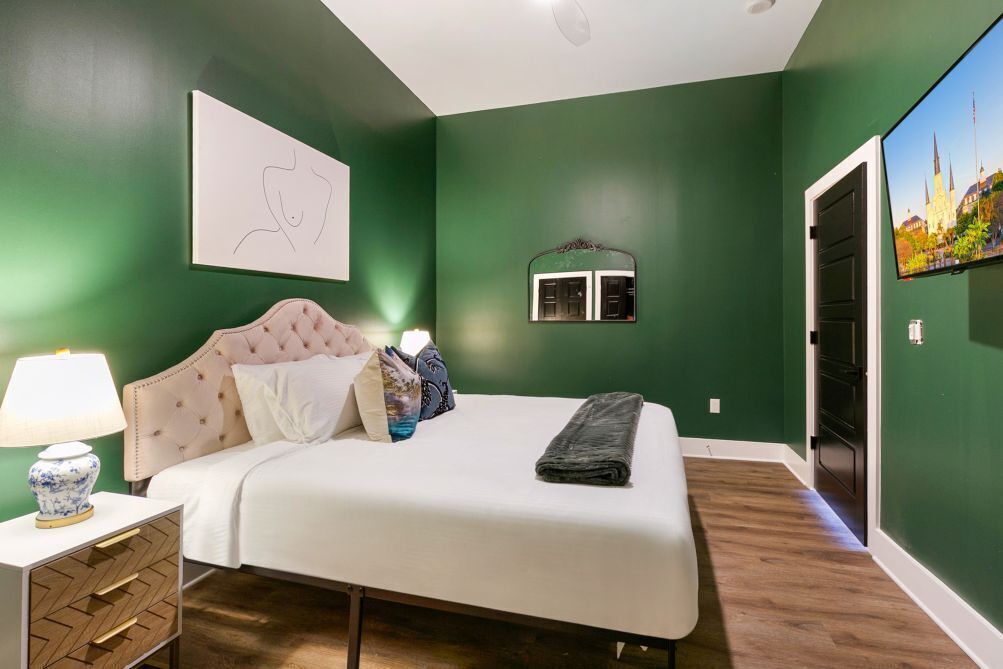 A bedroom with a bed, a nightstand, a lamp, a mirror, and a wall-mounted TV.