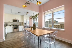 Una cocina moderna con armarios blancos, electrodomésticos de acero inoxidable y un comedor con mesa de madera y sillas transparentes.