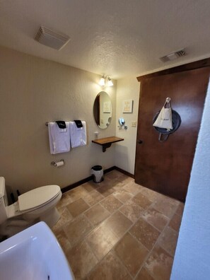 Une salle de bain avec des toilettes, un lavabo et un miroir. Il y a des serviettes accrochées au mur et une poubelle.