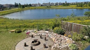 A lakeside patio with a fire pit, surrounded by a wooden fence and a stone pathway. - Best home with lakeview access peace and quite place for family (Edmonton)